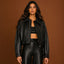 Person wearing a black leather jacket and pants against a brown background