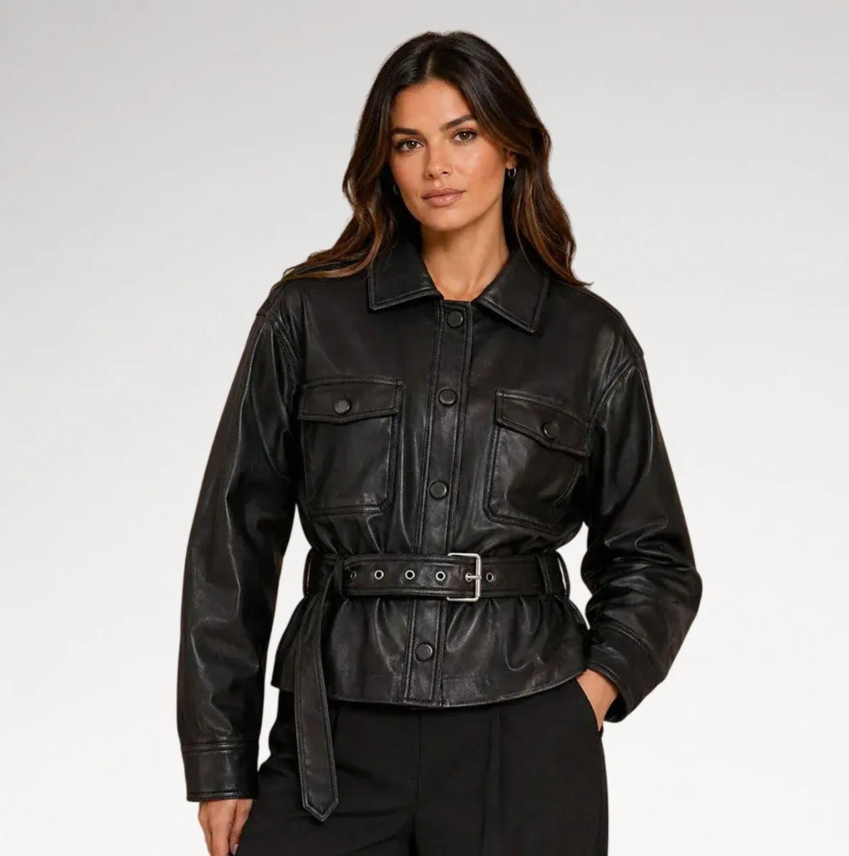 A woman modeling a black leather jacket with a button-up front, flap chest pockets, and a matching self-tie belt, photographed against a light gray studio background.