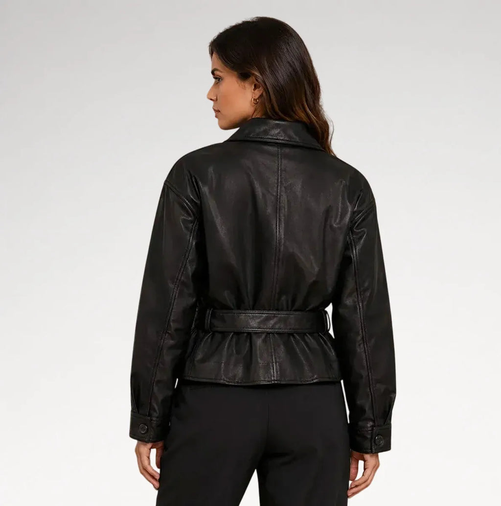 A woman shown from the back wearing a black leather jacket with a belted waist and black trousers, photographed against a light gray studio background.