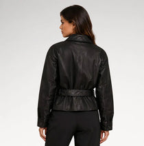 A woman shown from the back wearing a black leather jacket with a belted waist and black trousers, photographed against a light gray studio background.