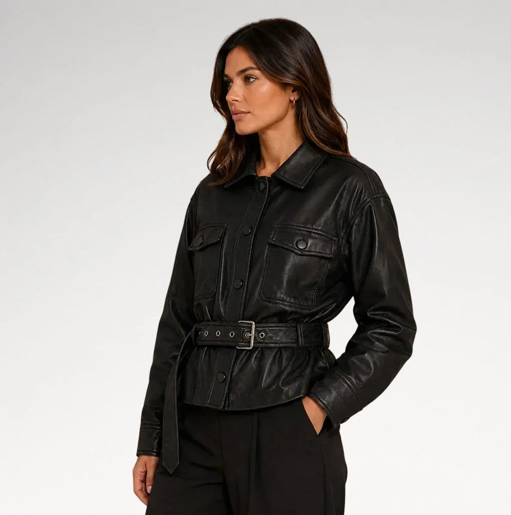 A woman wearing a black leather jacket with a matching belt, styled with black trousers against a light gray studio background.