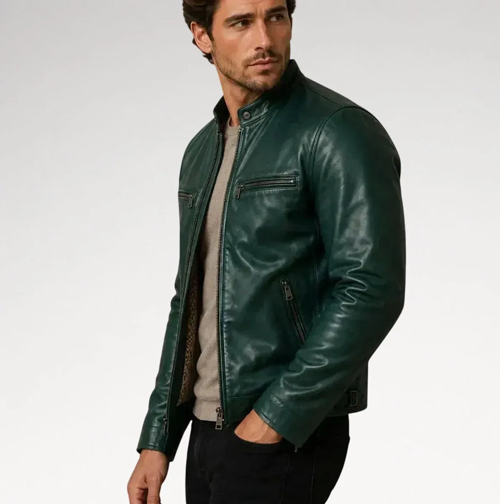 A man wearing a dark green leather jacket over a light gray sweater and black pants, photographed against a plain light gray studio background.