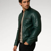 A man wearing a dark green leather jacket over a light gray sweater and black pants, photographed against a plain light gray studio background.