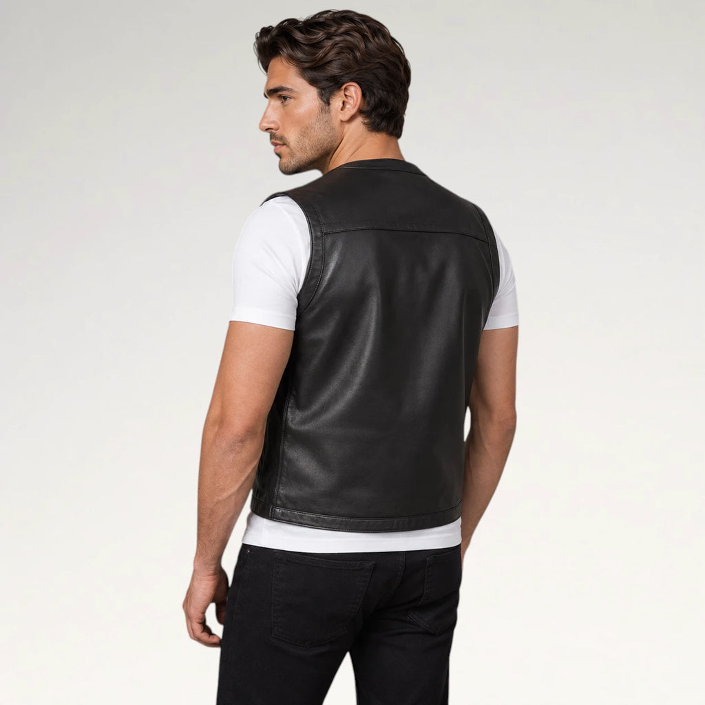 A man wearing a black leather vest over a white t-shirt and black pants, shown from a three-quarters back view against a light gray studio background.