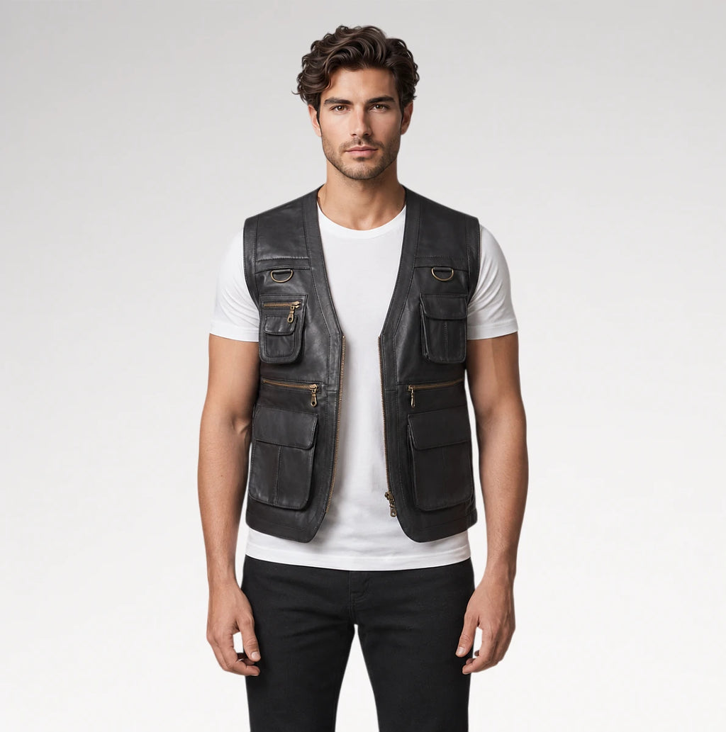 A man modeling a black leather utility vest with multiple zippered and buttoned pockets over a white t-shirt and black pants, shot against a light gray studio background.