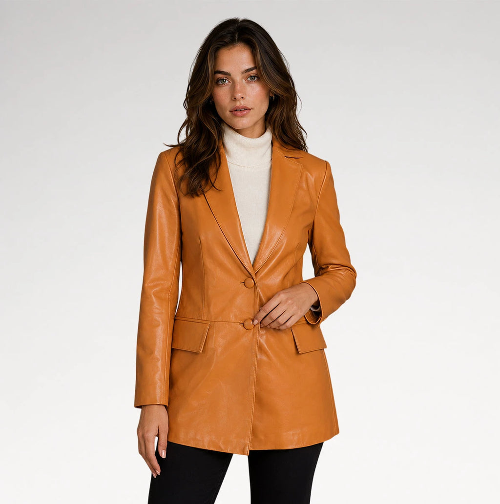 A woman modeling a tan faux-leather blazer over a white turtleneck and black pants, photographed against a light gray studio background.