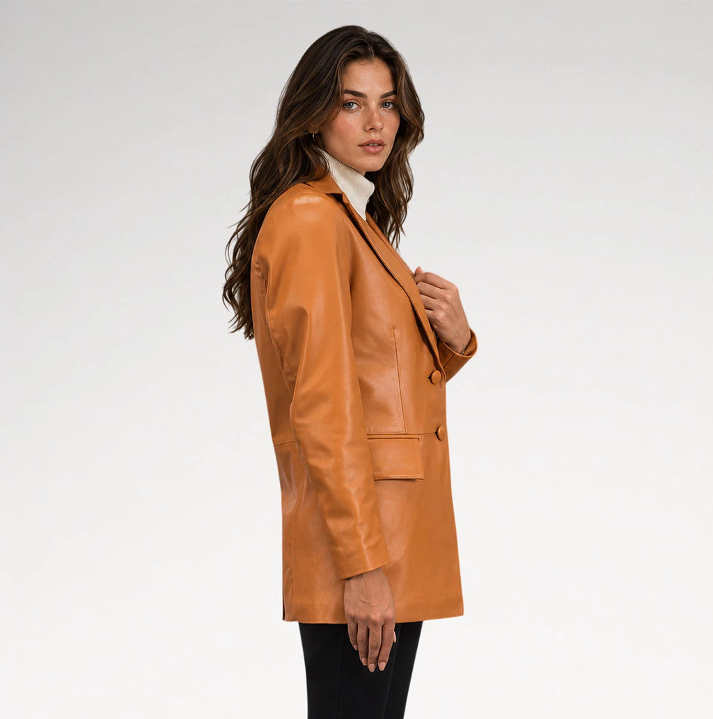 A woman wearing a camel brown leather blazer over a white turtleneck and black pants, photographed from the side against a light gray studio background.