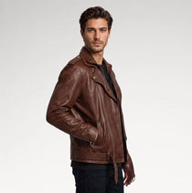 A man wearing a brown leather motorcycle jacket, styled over a black shirt and dark jeans, photographed against a clean light gray studio background.