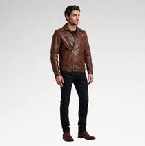 A man modeling a brown leather moto jacket, paired with black jeans and brown boots, standing against a light gray studio background.