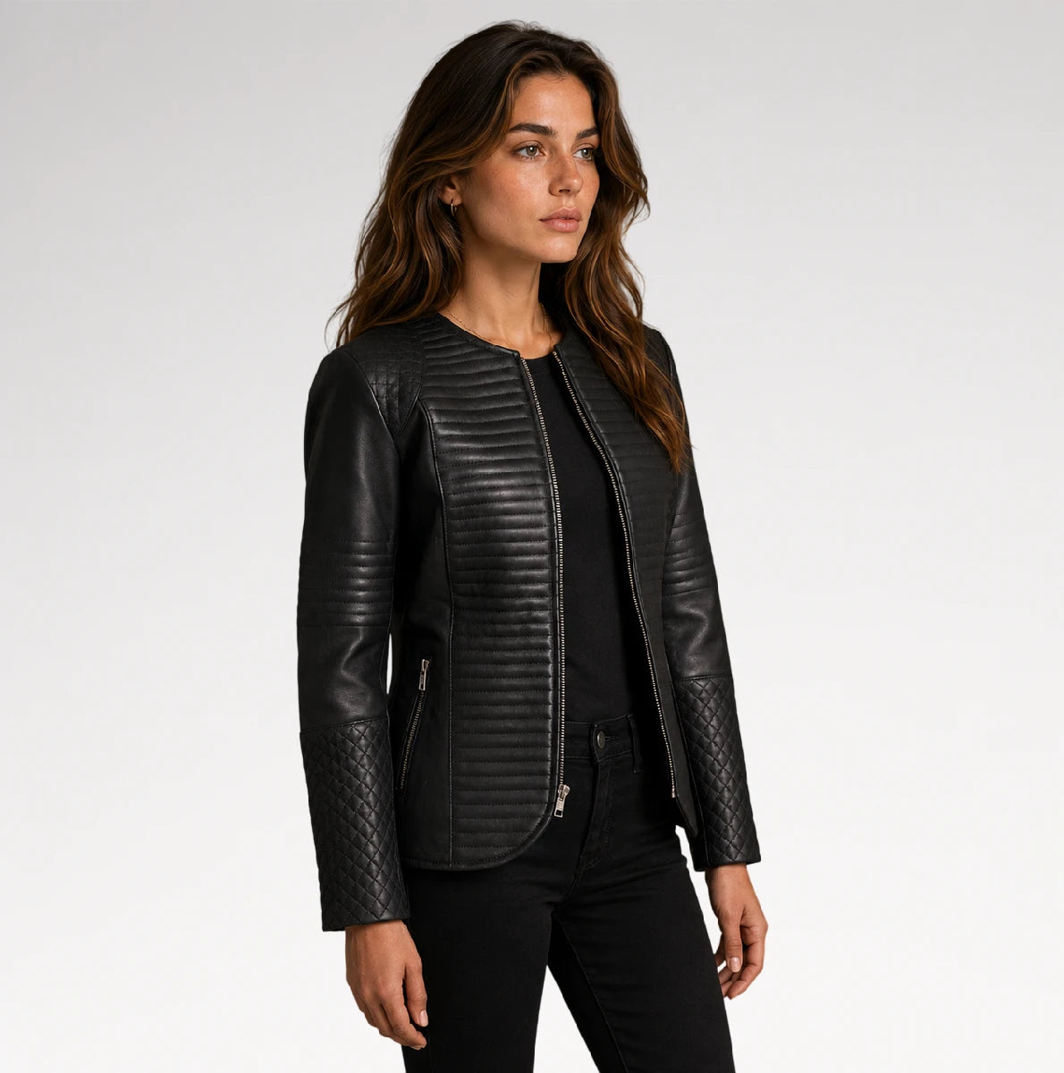 A woman modeling a black faux leather jacket with quilted sleeves and a ribbed front panel, paired with a black top and black pants, against a light gray studio background.