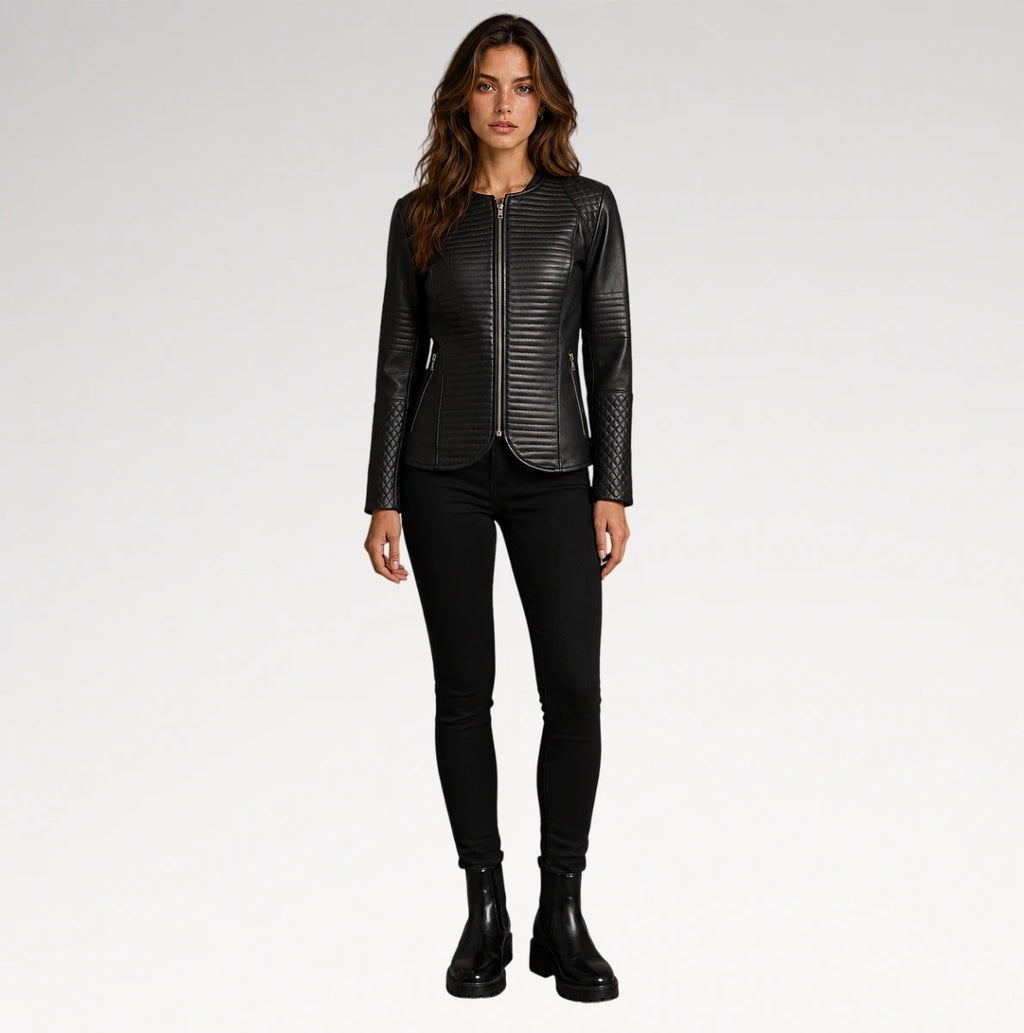 A woman modeling a black textured leather jacket with a front zipper, paired with black skinny pants and black ankle boots, against a light gray studio background.