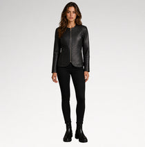 A woman modeling a black textured leather jacket with a front zipper, paired with black skinny pants and black ankle boots, against a light gray studio background.