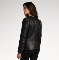 A woman shown from the back wearing a black leather jacket with quilted sleeve panels, photographed against a plain light gray studio background.