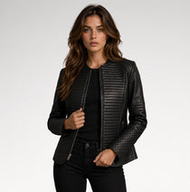A woman modeling a black faux leather jacket with quilted and ribbed textures, styled over a black top and black pants against a light gray studio background.
