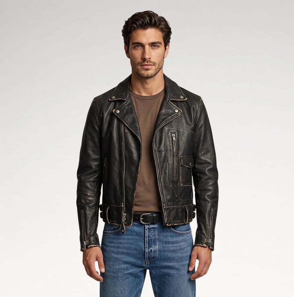 A man wearing a black leather motorcycle jacket over a brown t-shirt and blue jeans, standing against a light gray studio background.