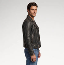 A man wearing a distressed black leather biker jacket and blue jeans, shown in profile against a light gray studio background.