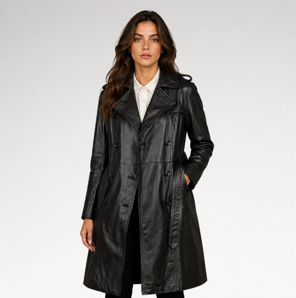 A woman modeling a black leather trench coat over a white collared shirt, photographed against a clean light gray studio background.