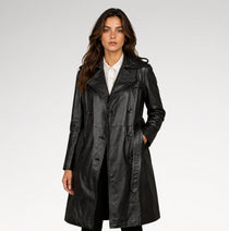 A woman modeling a black leather trench coat over a white collared shirt, photographed against a clean light gray studio background.