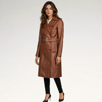 A woman modeling a brown faux-leather trench coat with a matching belt and silver buckle, paired with black pants and heels, against a plain white studio background.