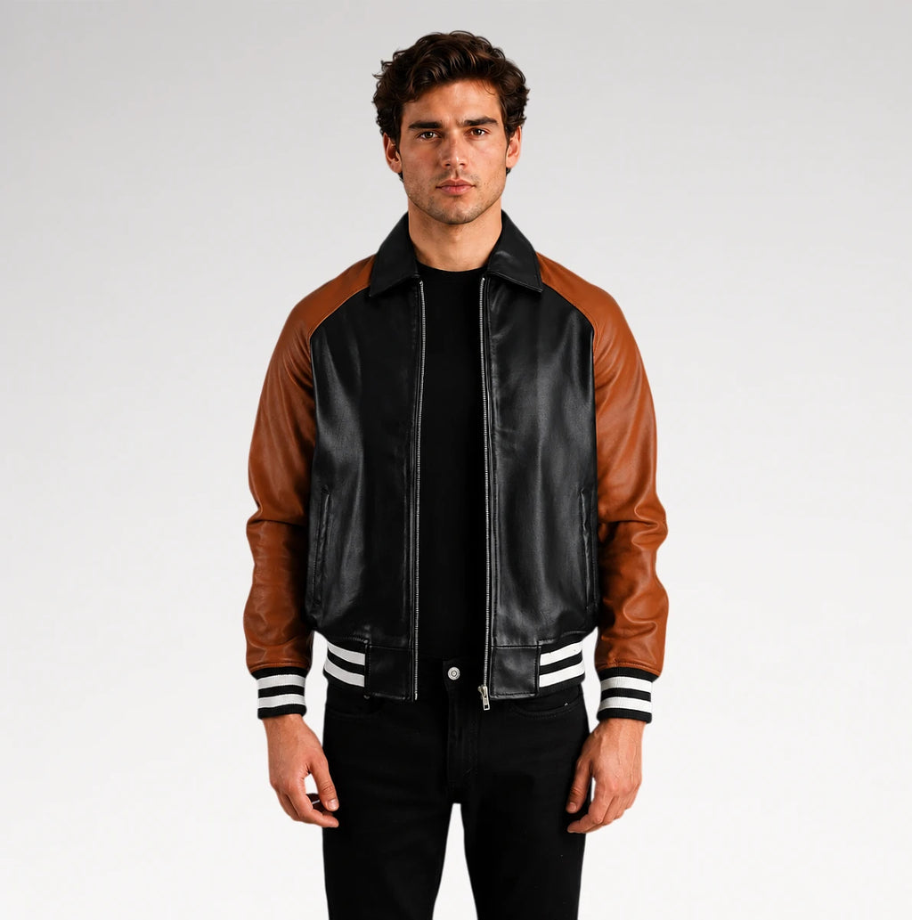 A man wearing a black and brown leather varsity-style jacket with white striped ribbed cuffs and collar, standing against a light gray studio background.