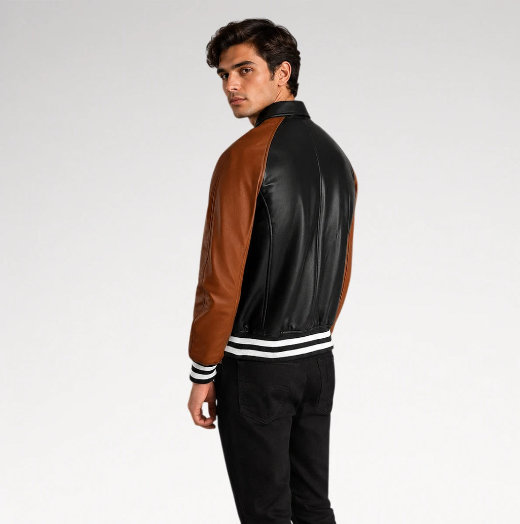 A man wearing a black and brown leather varsity-style jacket with white striped ribbed cuffs and hem, shown from a side-back angle against a light gray studio background.