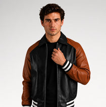 A man wearing a brown and black leather varsity-style jacket with white striped ribbed cuffs and hem, posing against a light gray studio background.