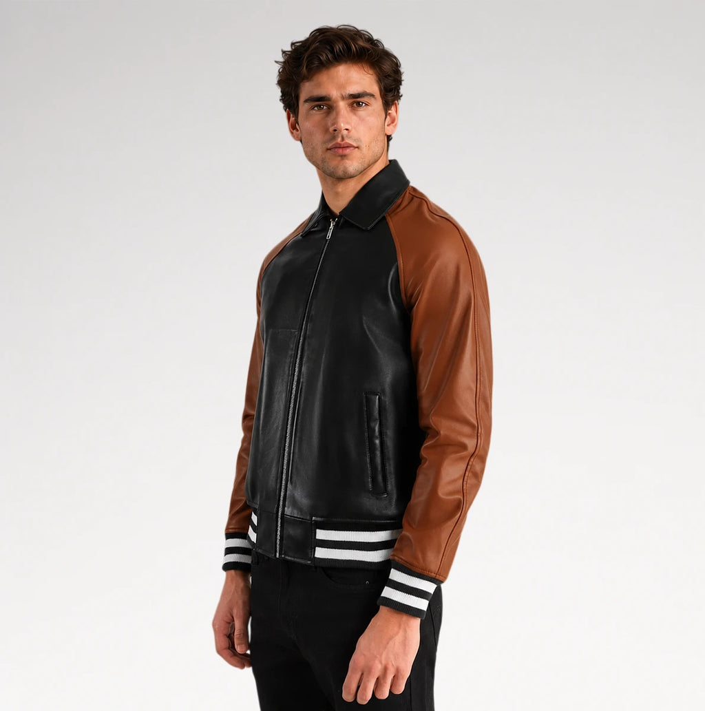 A man wearing a two-tone leather bomber jacket with black front panels and brown sleeves, featuring white stripes on the ribbed collar, cuffs, and hem, set against a plain light gray background.