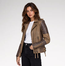 A woman modeling a brown faux leather moto jacket with quilted and textured sleeve panels, worn over a white t-shirt and black jeans, against a light gray studio background.