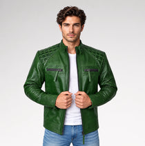 A man wearing a dark green faux leather motorcycle jacket with quilted chest panels, zippered pockets, and a white t-shirt underneath, standing against a light gray studio background.