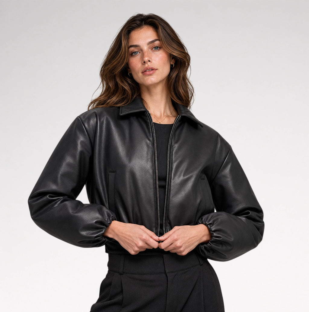 A woman wearing a black faux-leather bomber jacket with a stand-up collar and elasticized cuffs, posing against a light gray studio background.
