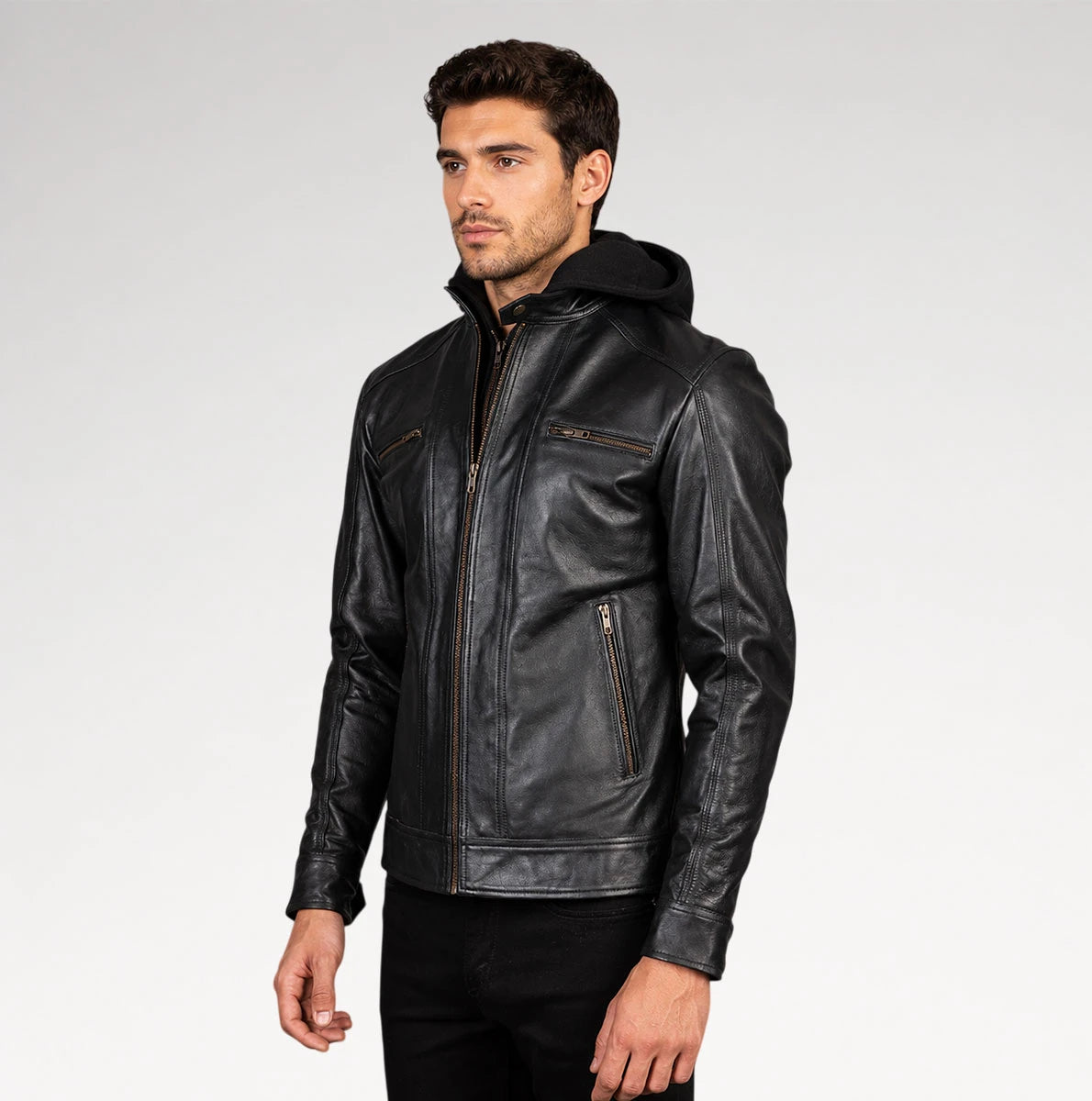 A man wearing a black leather hooded jacket with zippered pockets, standing against a light gray studio background.