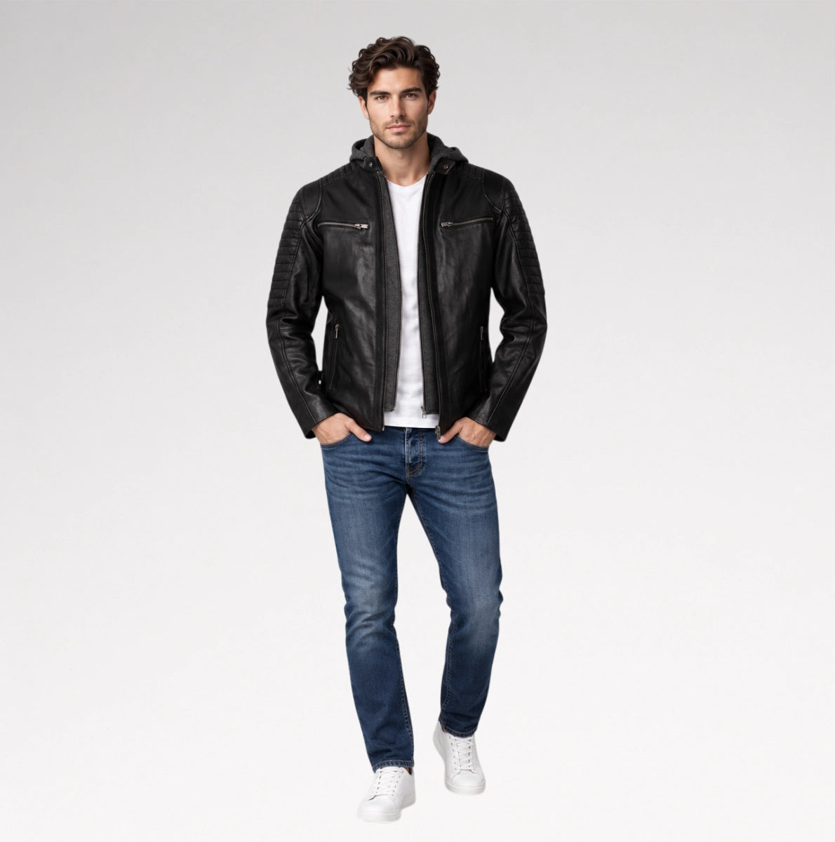 A man modeling a black leather jacket with a zippered hood, worn over a white t-shirt and blue jeans, on a light gray studio background.