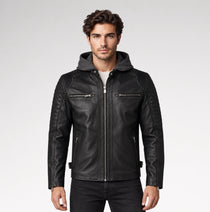 A man wearing a black leather hooded biker jacket with quilted sleeves and silver zippers, paired with a white t-shirt and black jeans, against a light gray studio background.