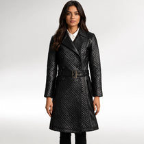 A woman modeling a black quilted leather coat with a matching belt, worn over a white collared shirt, against a light gray studio background.
