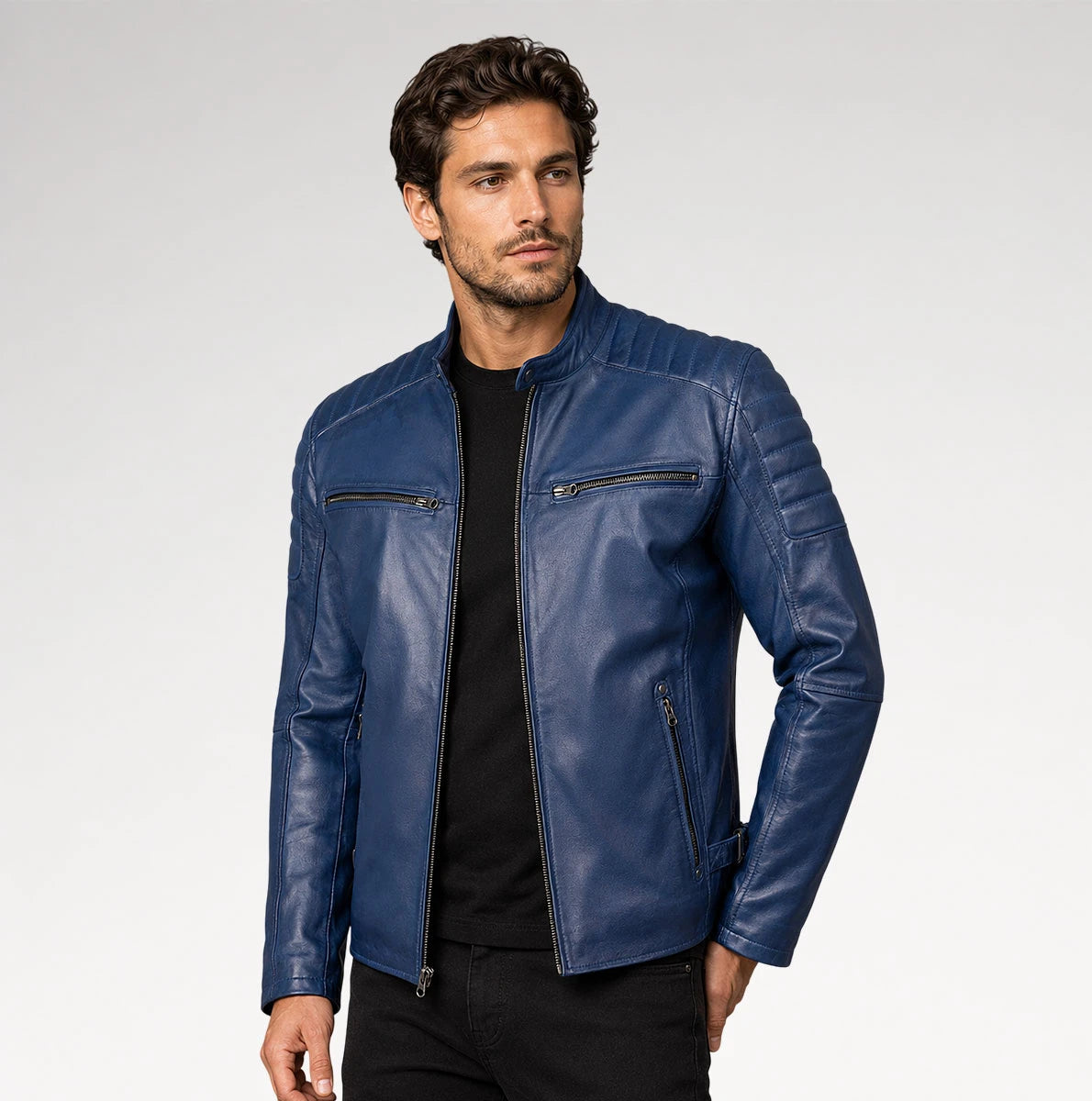 A man wearing a blue leather jacket over a black shirt and black pants, standing against a light gray studio background. Main image