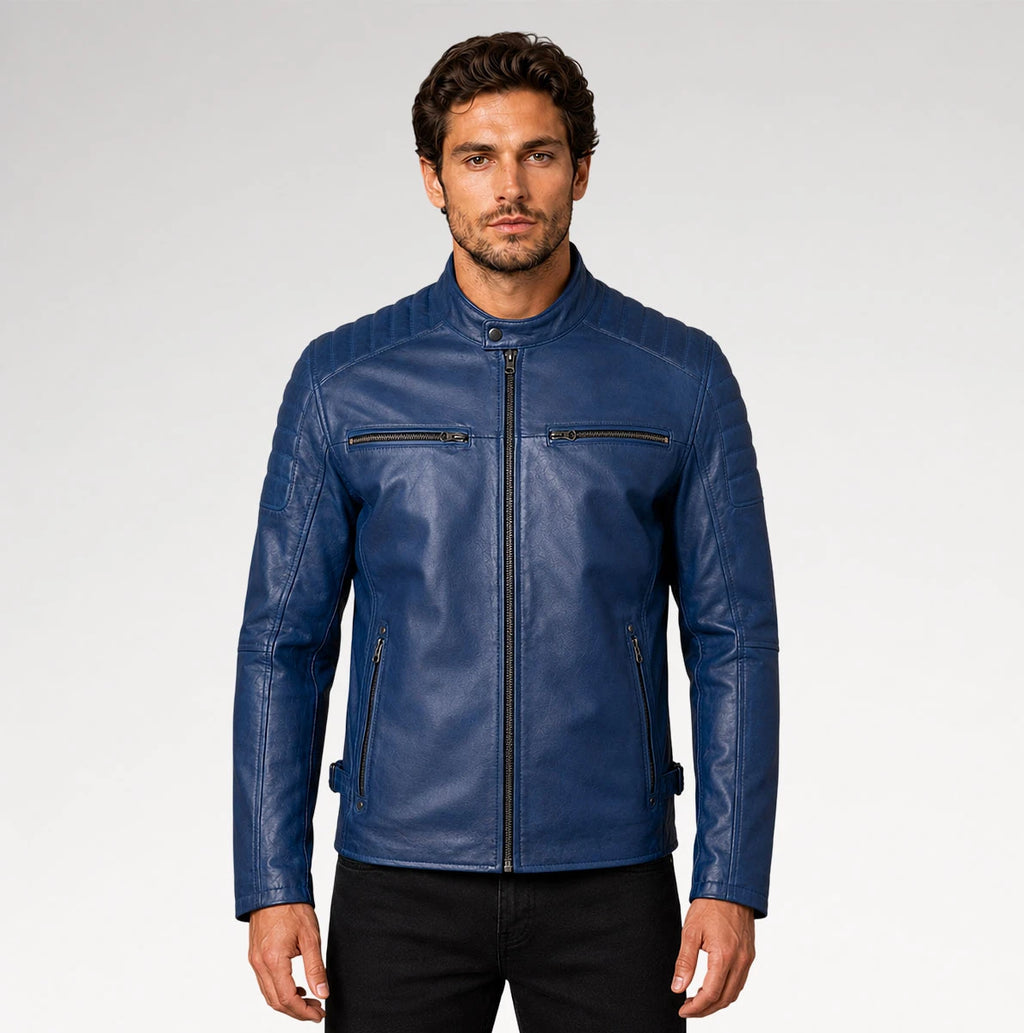 A man wearing a blue leather jacket with a stand collar, zippered front, and zippered chest pockets, paired with black pants, photographed against a light gray studio background.