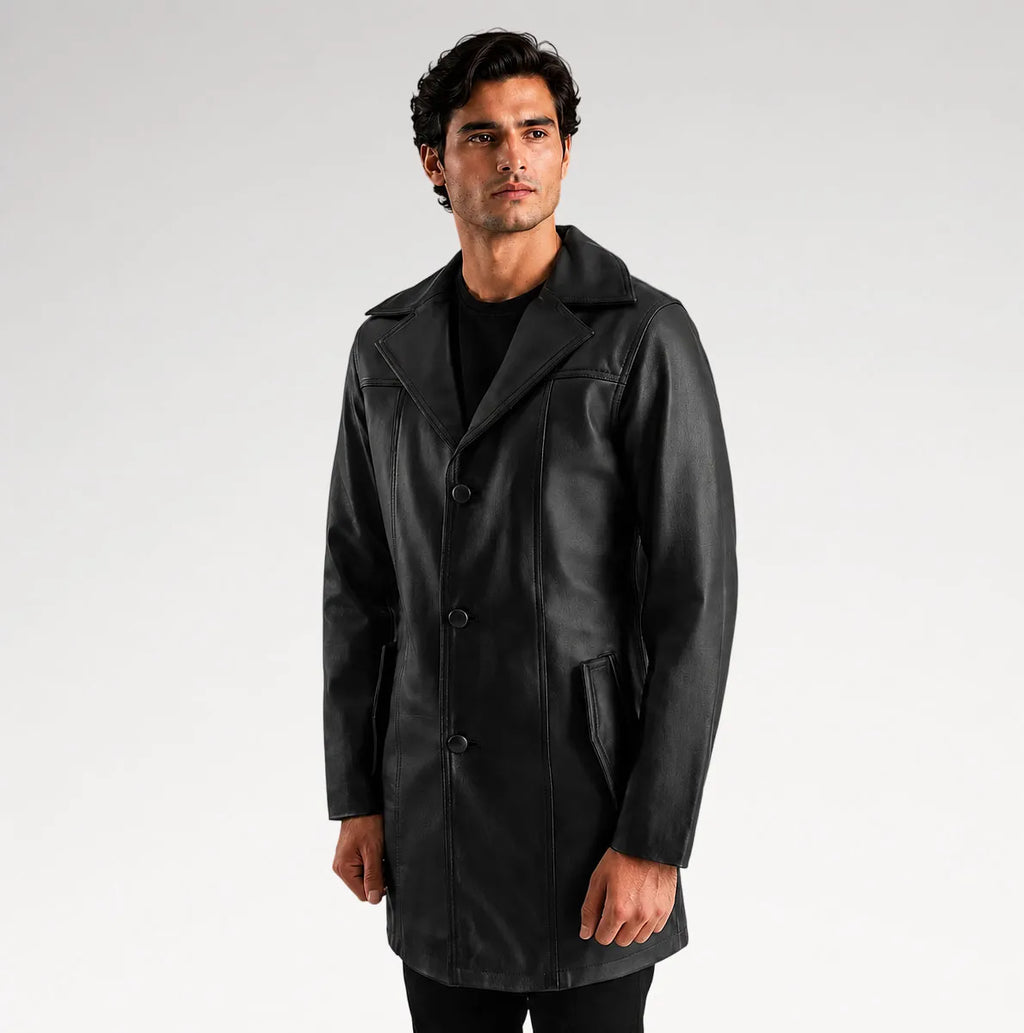 A man wearing a black leather-like coat over a black shirt, standing against a light gray studio background.