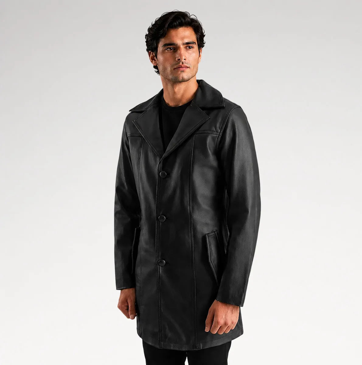 A man wearing a black leather-like coat over a black shirt, standing against a light gray studio background.
