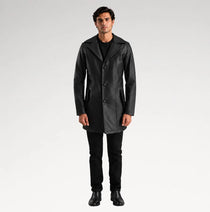 A man modeling a black leather-like coat over a black outfit, standing against a light gray studio background.