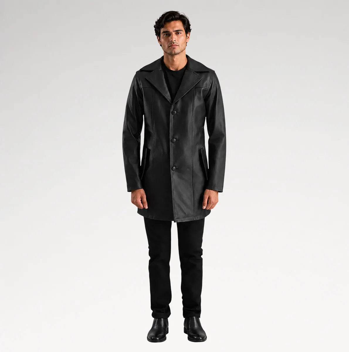 A man modeling a black leather-like coat over a black outfit, standing against a light gray studio background.