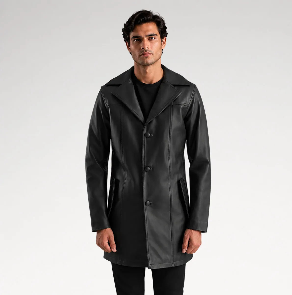A man modeling a black leather-like coat over a black outfit, standing against a light gray studio background.
