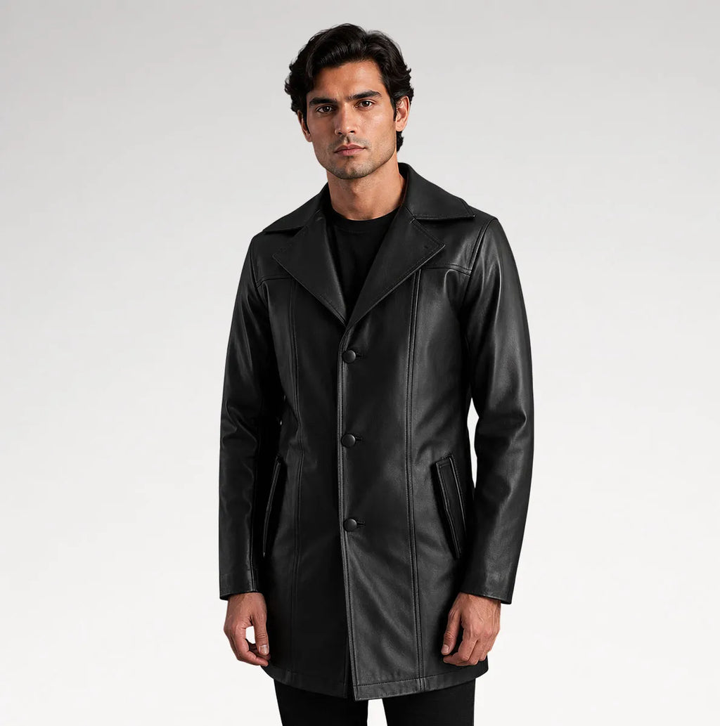 A man modeling a black leather-like coat over a black outfit, standing against a light gray studio background.