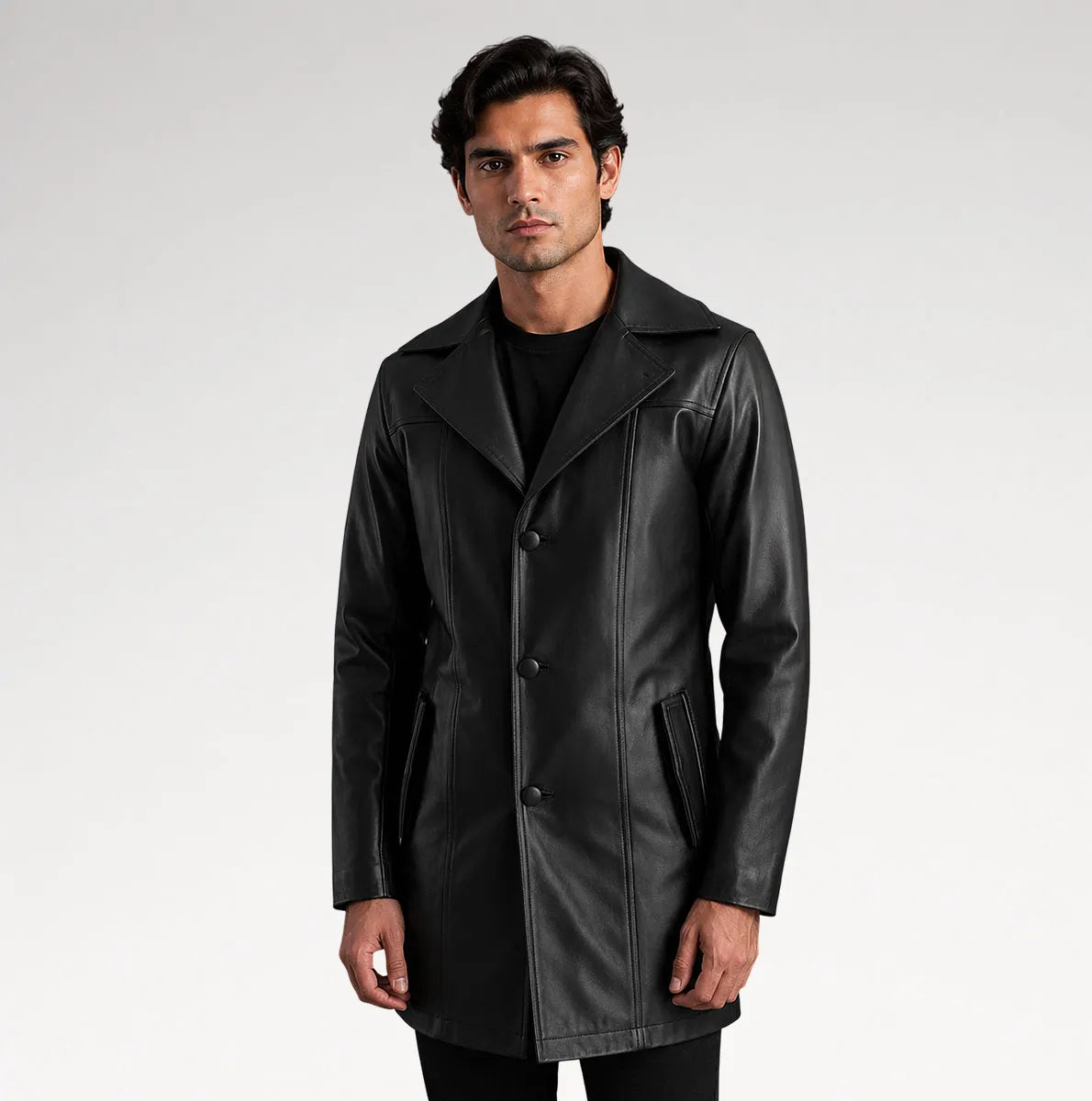 A man modeling a black leather-like coat over a black outfit, standing against a light gray studio background.