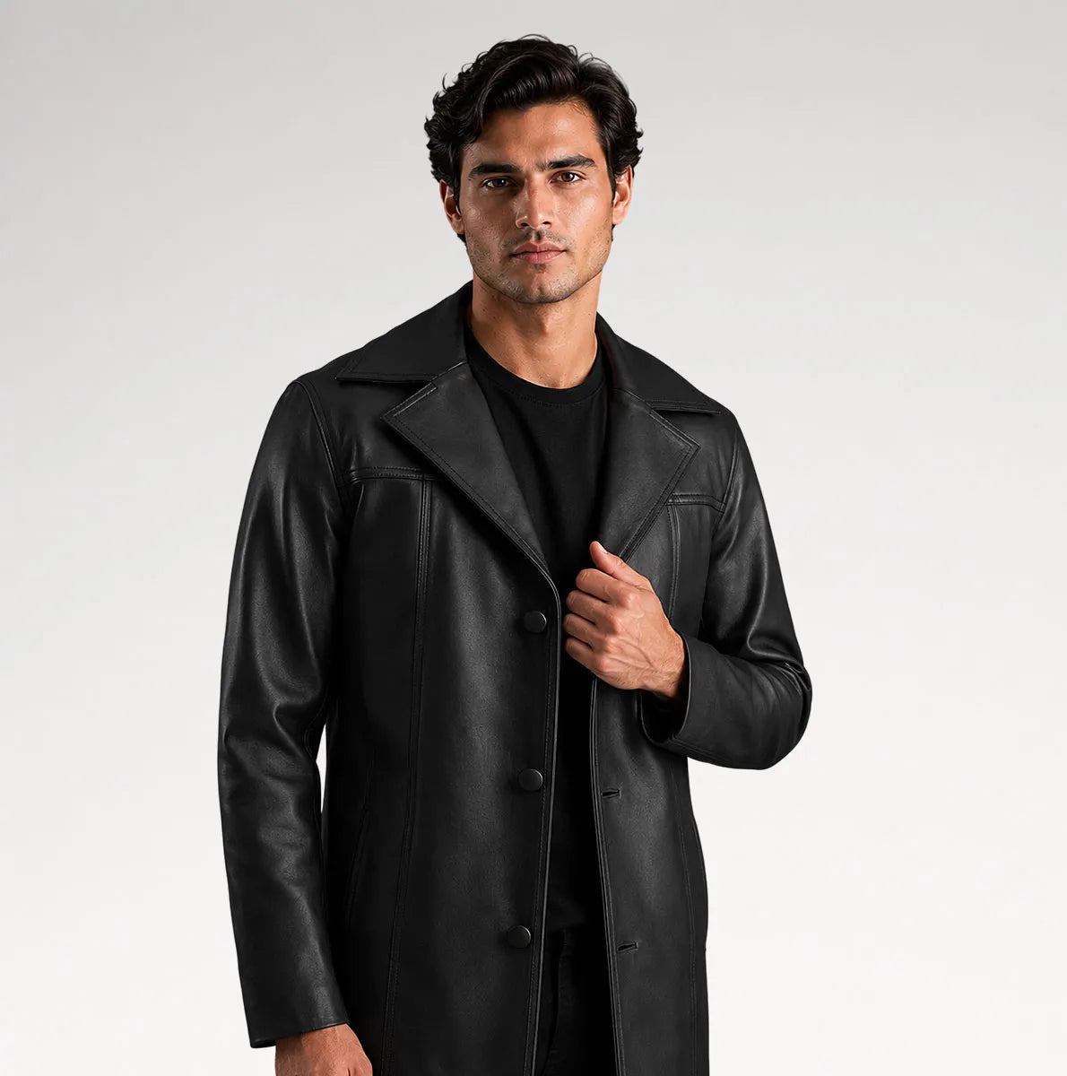 A man modeling a black leather-like coat over a black outfit, standing against a light gray studio background.