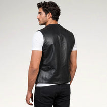 A man shown from the back wearing a black leather vest over a white t-shirt and black jeans, photographed against a light gray studio background.