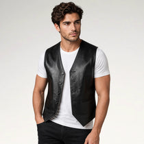 A man wearing a black leather vest over a white t-shirt and black jeans, standing against a light gray studio background.