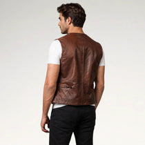 A man shown from the back wearing a brown leather vest over a white t-shirt and black pants, photographed against a light gray studio background.