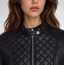 Close-up of a woman wearing a black quilted faux-leather moto jacket with a snap collar and front zipper.