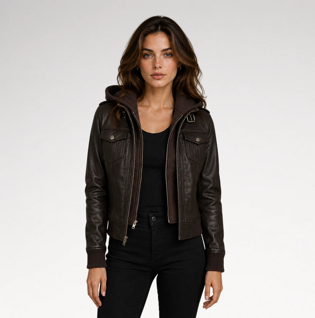 A woman modeling a dark brown faux-leather hooded jacket with a front zipper and flap chest pockets, paired with a black top and black pants, against a light gray studio background.