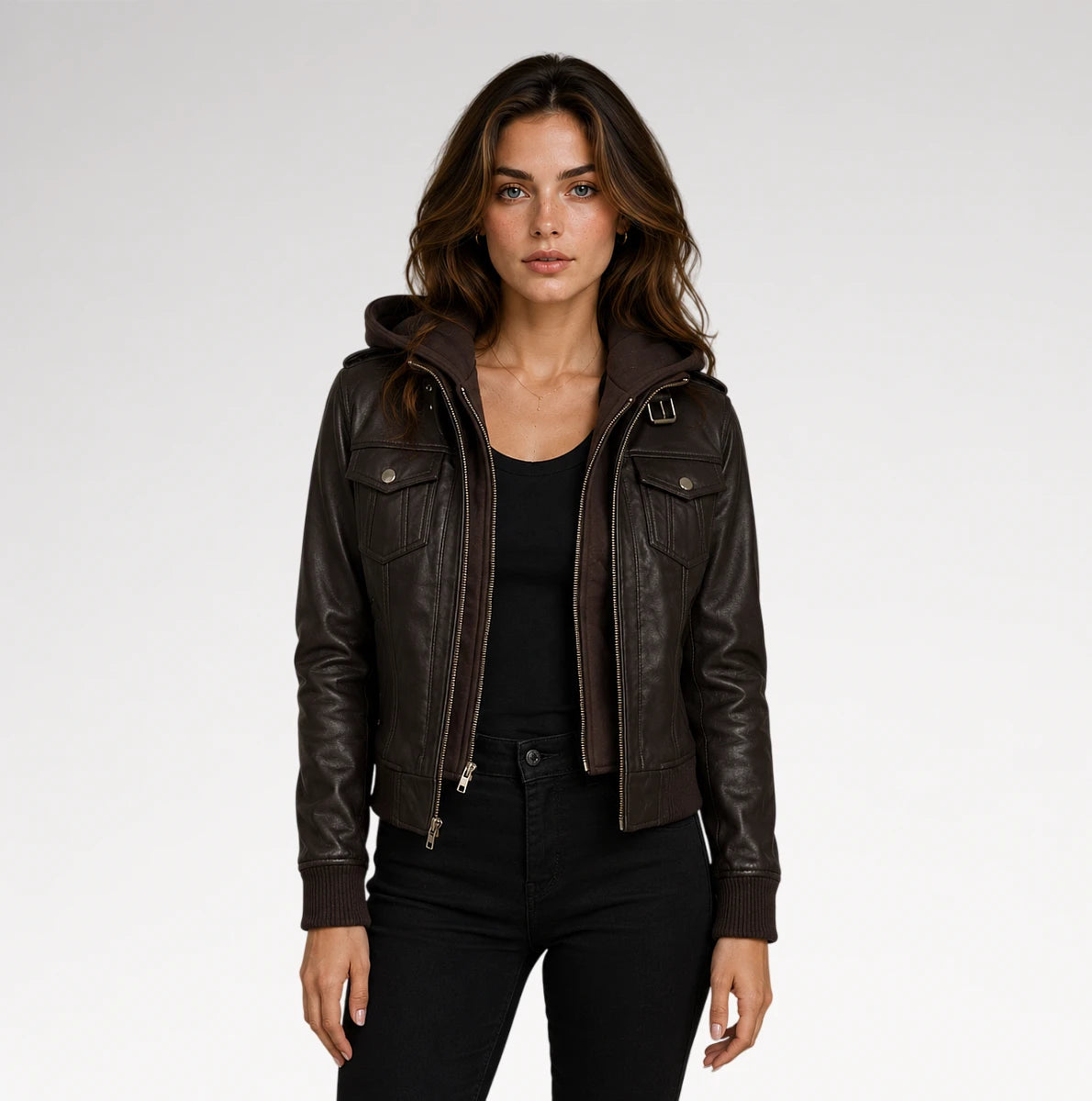 A woman modeling a dark brown faux-leather hooded jacket with a front zipper and flap chest pockets, paired with a black top and black pants, against a light gray studio background.